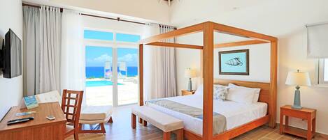 Una cama con dosel con vistas al mar, un escritorio con una silla y una mesita de noche con una lámpara.