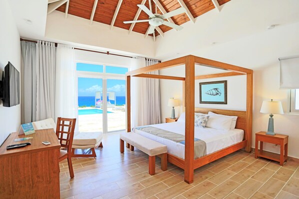 A four-poster bed with a view of the sea, a desk with a chair, and a small bedside table with a lamp.