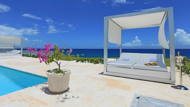 A poolside area with a white canopy, a lounge chair, and a potted plant with pink flowers. - Ocean Front Villa Deluxe 4 Bedroom (Sosúa)