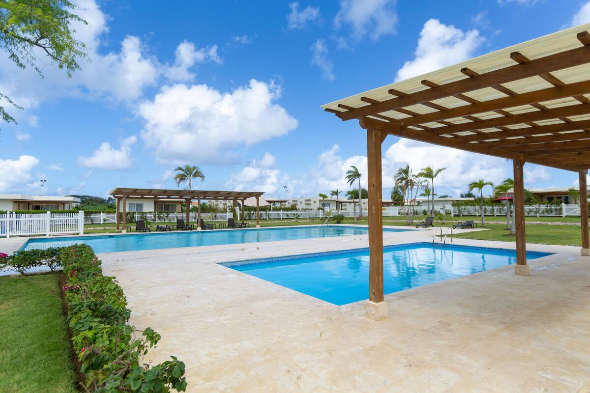 A swimming pool area with a pergola, palm trees, and a white fence.