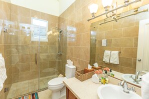 A modern bathroom with a glass-enclosed shower, a toilet, a sink, and a large mirror. - Sosua Ocean Village Properties by Calisto Stays (Sosúa)