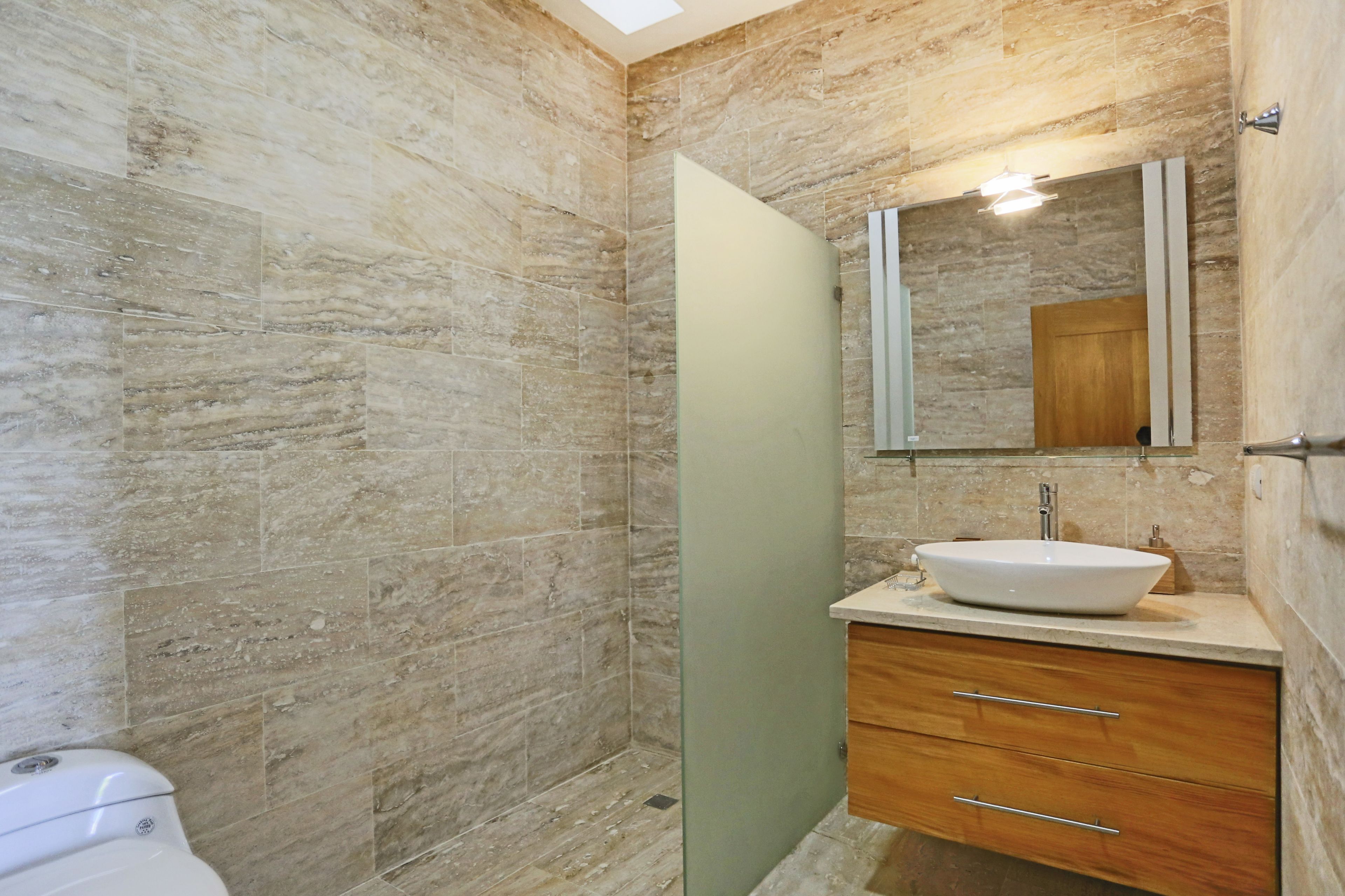 A bathroom with a marble wall, a white sink, a mirror, and a toilet.