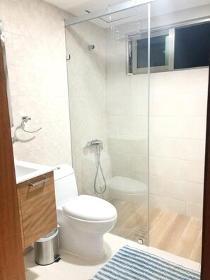 A modern bathroom with a glass shower enclosure, a white toilet, and a wooden vanity.