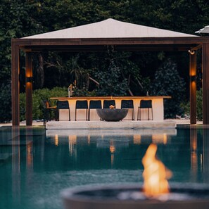 A pool with a fire feature, a covered seating area with chairs, and a table. - Mandarin Oriental, Desaru Coast (Bandar Penawar)