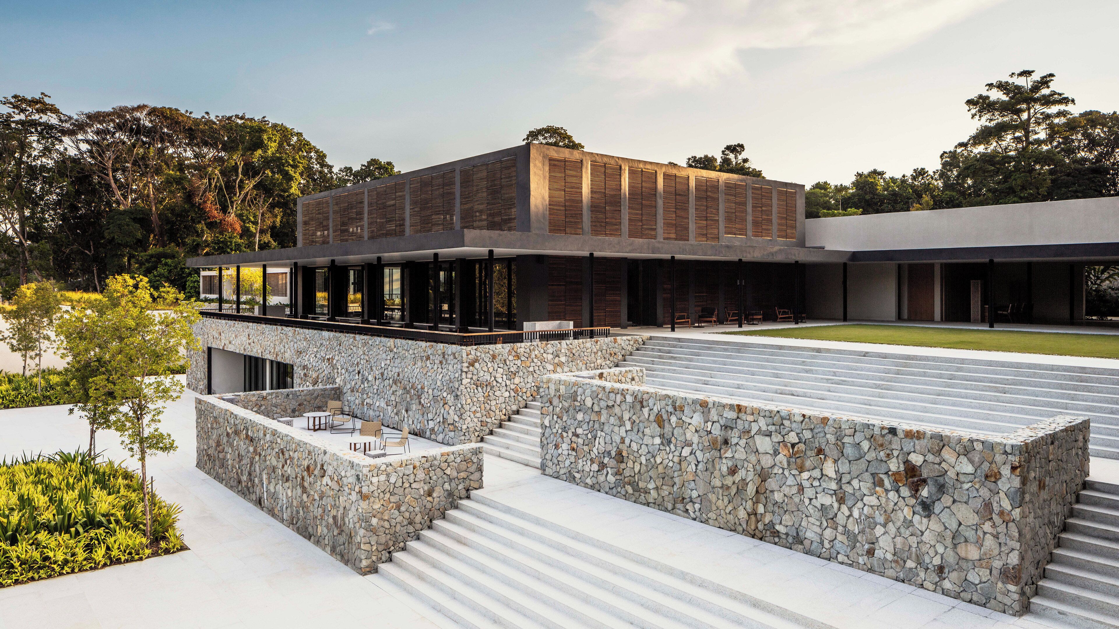 Un edificio moderno con fachada de piedra, zona de estar al aire libre y techo plano.
