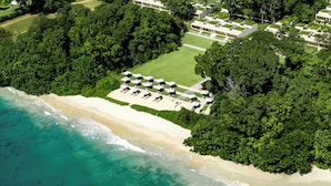 Een luchtbeeld van een kustresort met een strand, weelderige begroeiing en een rij strandparasols.