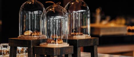 Three glass domes with pastries inside, placed on wooden stands on a marble surface.