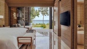 Een moderne slaapkamer met een groot bed, een kleiner bed, een televisie en een balkon met uitzicht op zee.