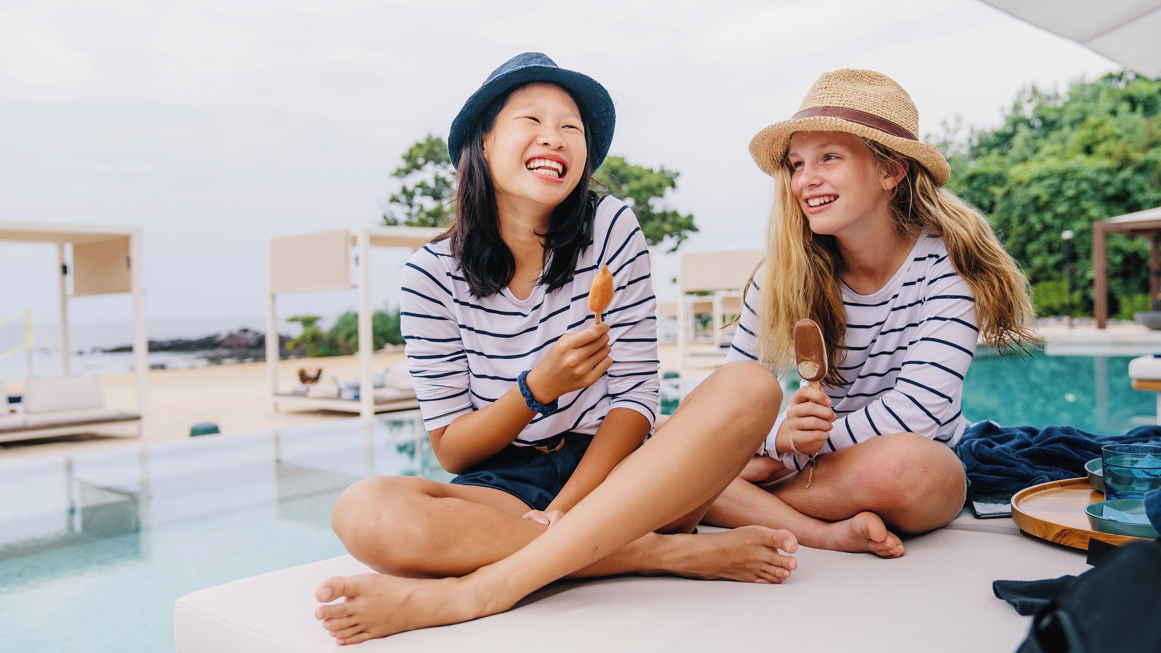 Two people sitting by a poolside with a view of the beach and a clear sky.