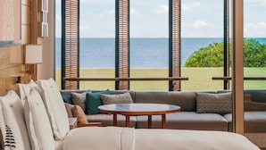Habitación con un amplio ventanal con vista al mar, un sofá, una pequeña mesa redonda y una cama con vistas.