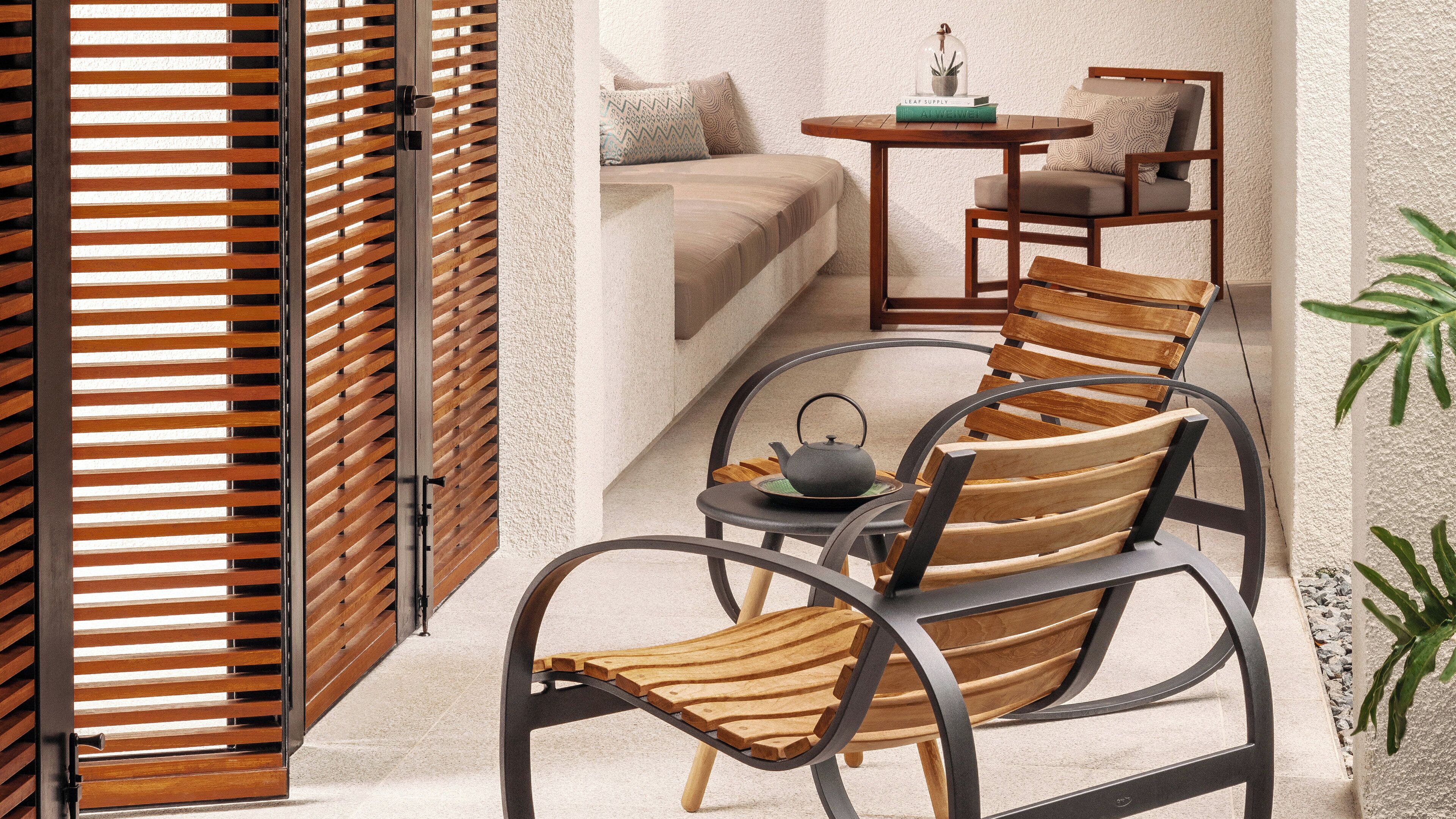 A cozy room with a wooden chair, a small table with a teapot, and a sofa with patterned cushions.