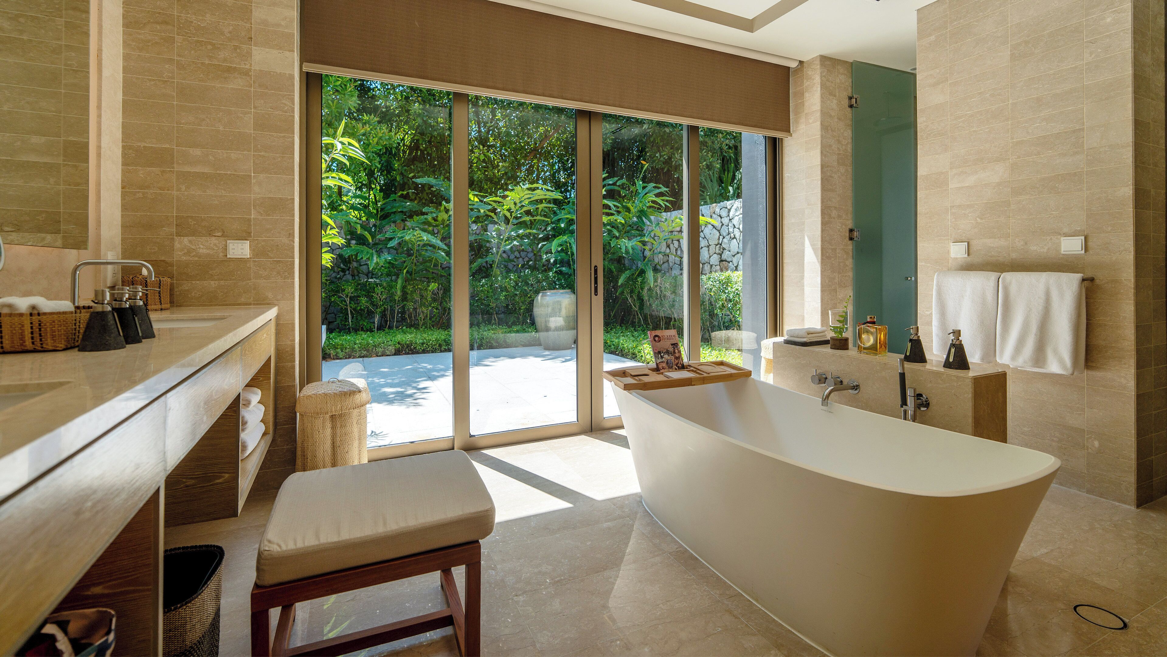 A modern bathroom with a freestanding bathtub, a vanity with a mirror, and a large window offering a view of greenery.