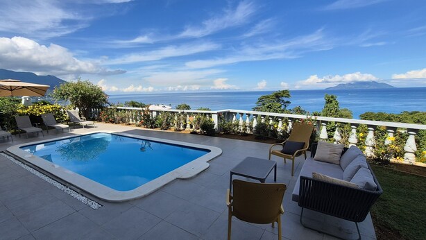A pool area with lounge chairs and a view of the ocean.