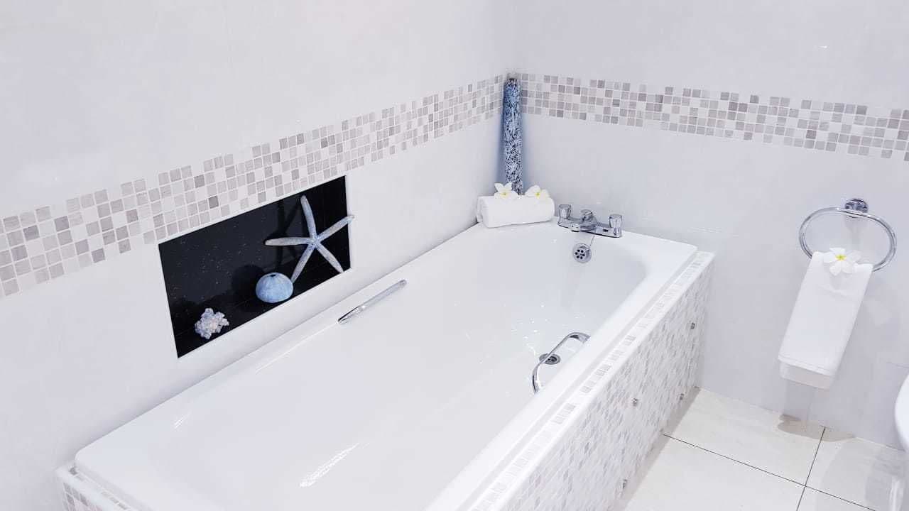 A modern bathroom with a large bathtub, a small window with a starfish decoration, and a tiled backsplash.