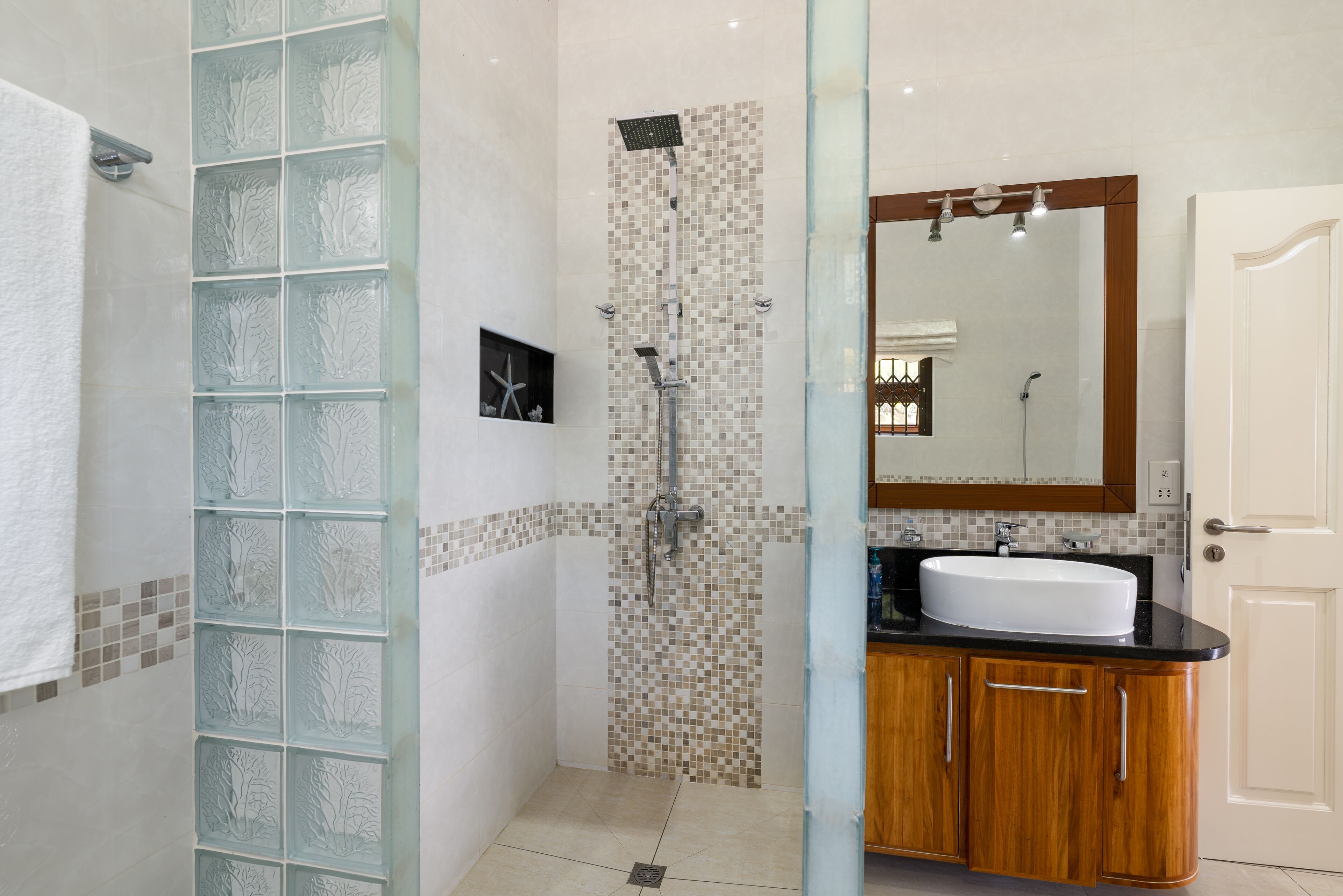 Un baño con cabina de ducha de vidrio, pared de ducha azulejada, lavamanos con tocador de madera y un espejo grande.
