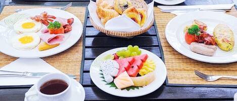 A breakfast setting with plates of eggs, bacon, pastries, and fruit on a wooden table.