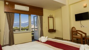 Habitación de hotel con cama, televisión, ventana con vistas a montañas y aire acondicionado.
