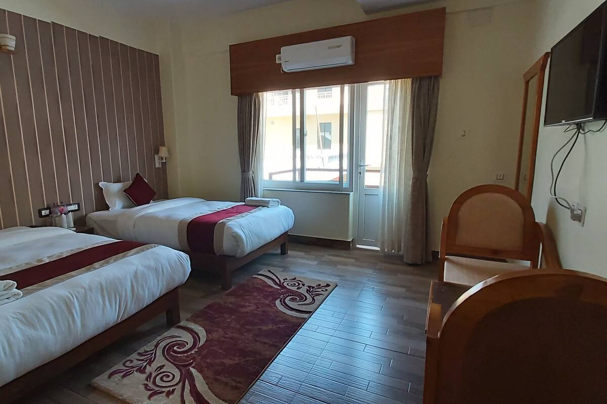Una habitación de hotel con dos camas, televisión, aire acondicionado y una ventana con cortinas.
