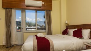 Una habitación de hotel con una cama, un ventanal con vistas a la montaña y un equipo de aire acondicionado.