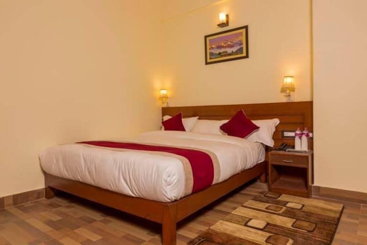 Habitación de hotel con cama de madera, dos mesitas de noche, una lámpara de noche, un cuadro en la pared y una alfombra estampada.