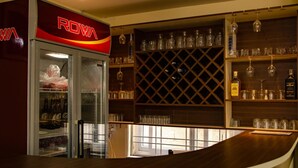 Una zona de bar con un refrigerador, estantes con botellas y vasos, y una barra de madera.