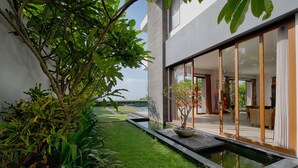 Een modern huis met een verzorgde tuin, een kleine waterpartij en grote glazen deuren die leiden naar de binnenruimte.