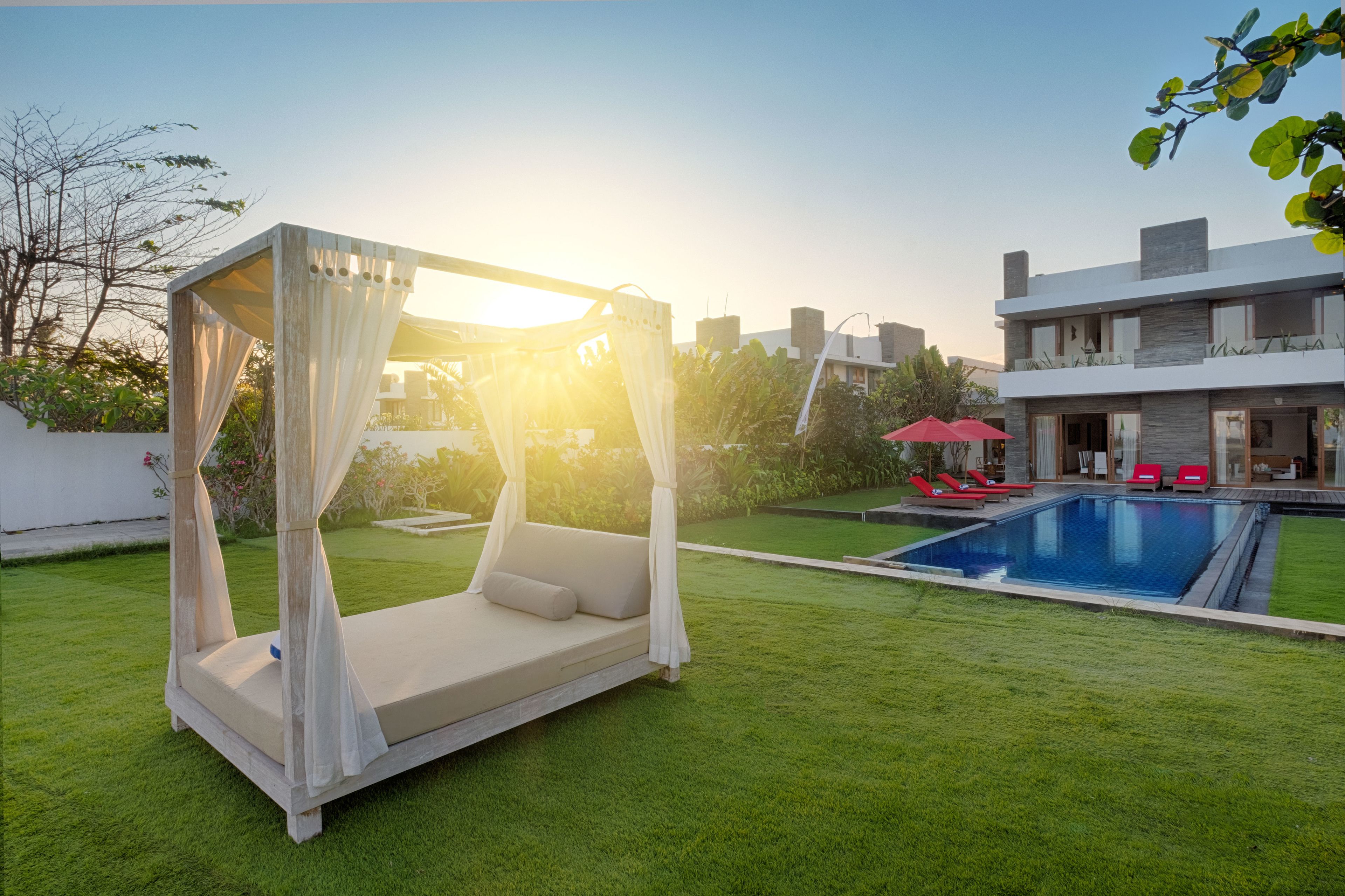 Un área moderna para relajarse al aire libre, con una cama con dosel, una piscina y un césped bien cuidado.