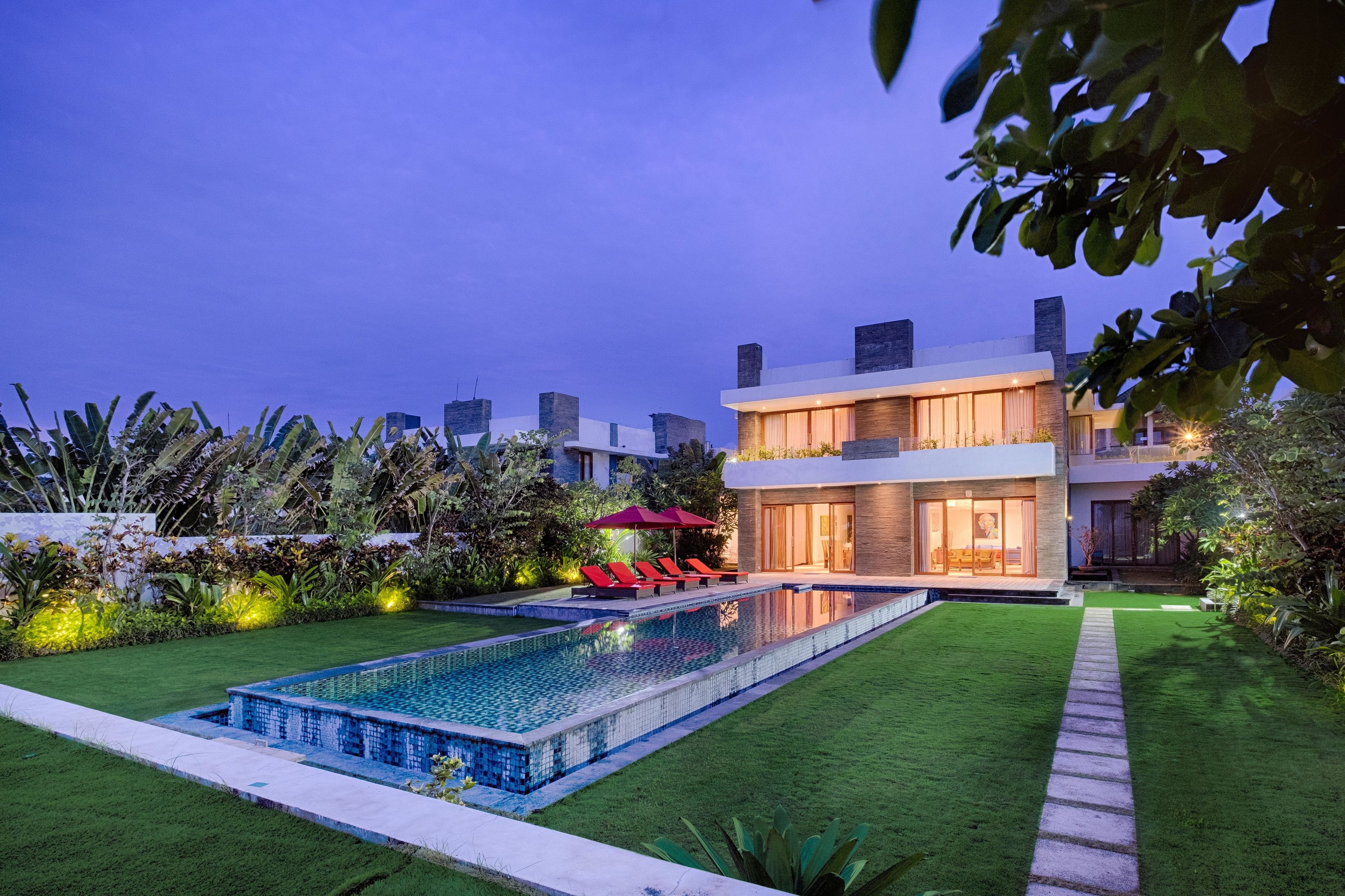 A modern two-story house with a swimming pool, a well-maintained lawn, and a red umbrella.