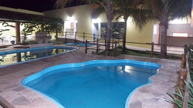 Una piscina con bordo in pietra, circondata da palme e un edificio con finestre illuminate.