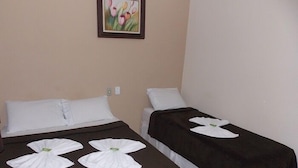 Due letti singoli con coperte marrone scuro e cuscini bianchi, un quadro con fiori appeso al muro e un asciugamano bianco ripiegato su ciascun letto.