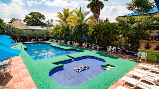 Un espace piscine comprenant plusieurs piscines, des chaises longues et des palmiers.