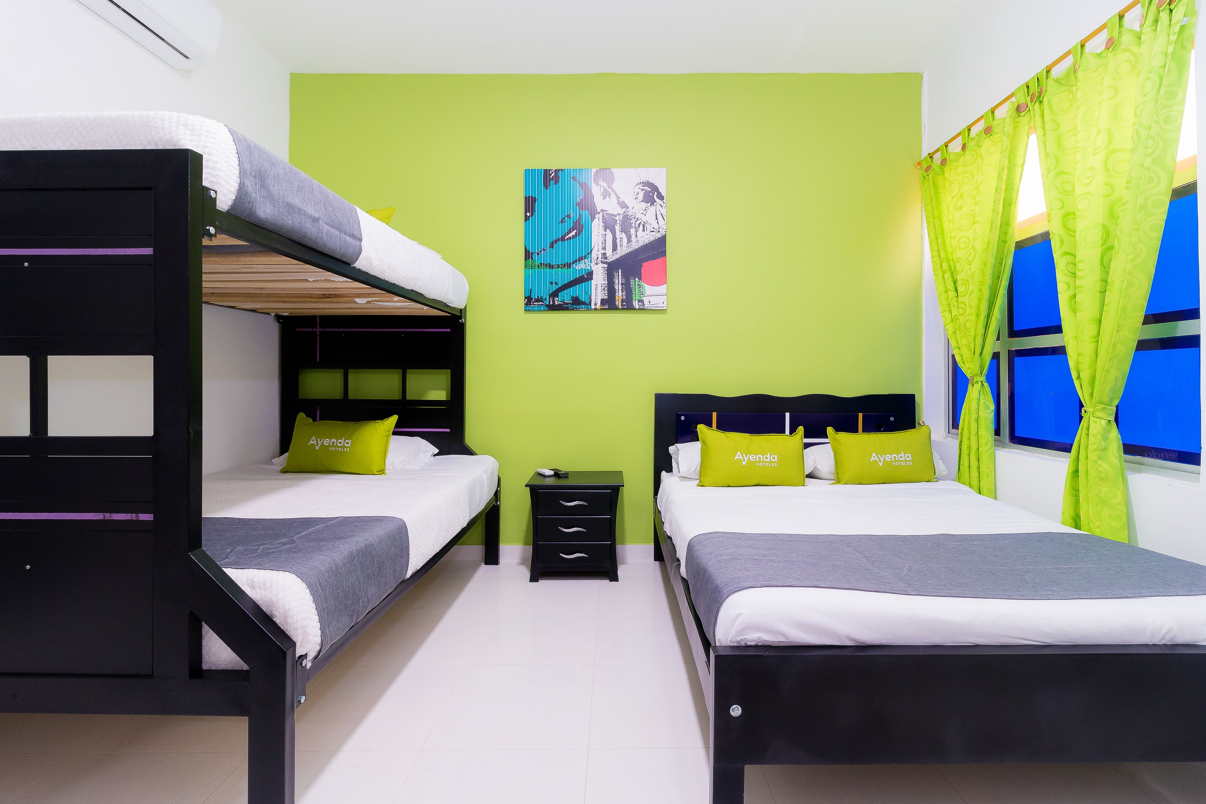 Una habitación de hotel con dos literas, una mesita pequeña, una mesilla de noche y una cama con cabecera.
