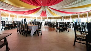 Un vaste espace intérieur aménagé en salle à manger, avec de nombreuses tables et chaises, un sol carrelé et un plafond décoré de tissus colorés.