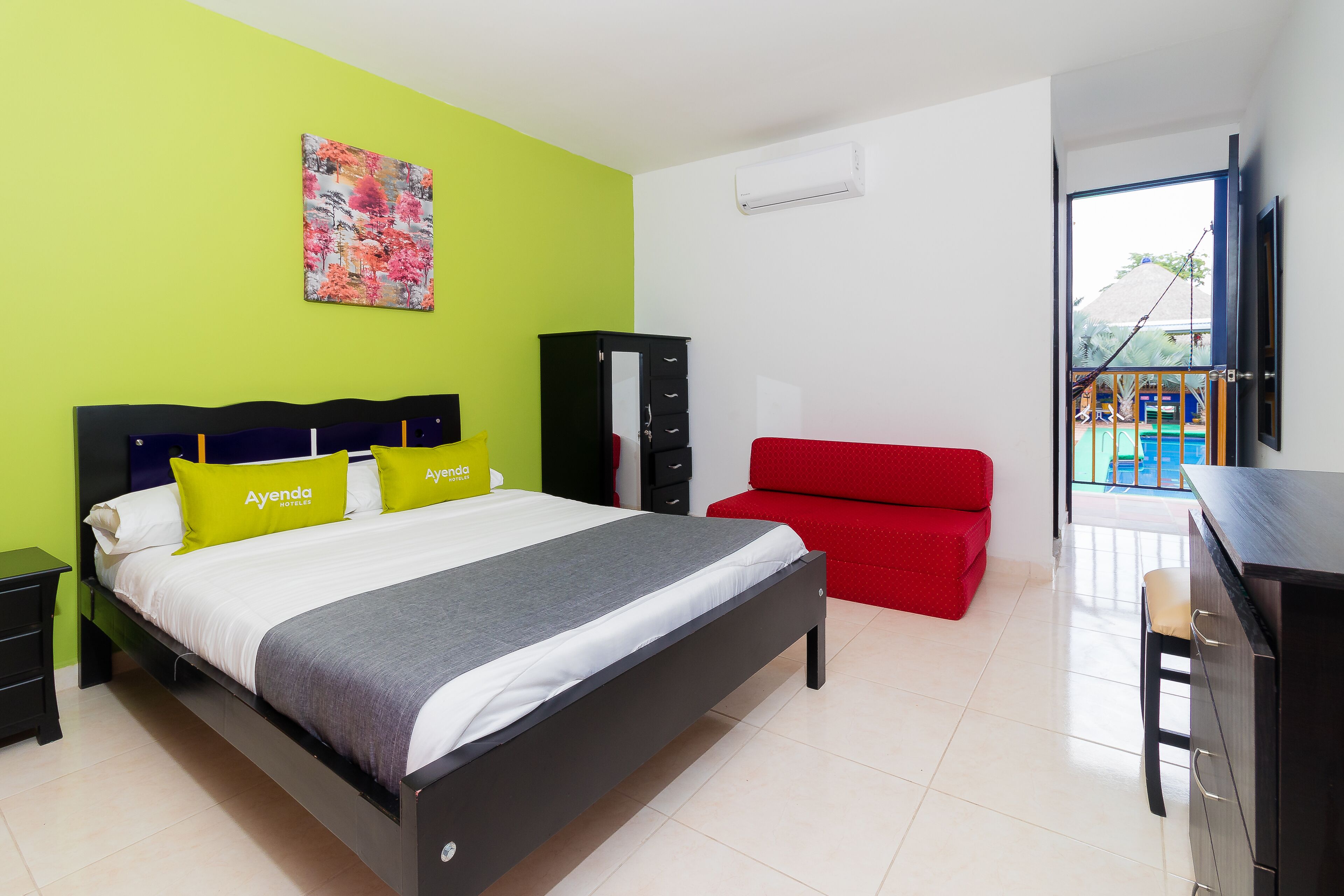 A hotel room with a bed, a red sofa, a desk, and a view of a pool.