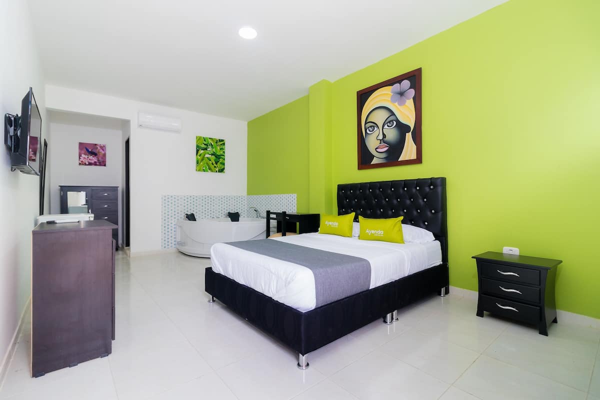 Un dormitorio con cama, mesitas de noche, cómoda y baño con bañera, además de una pared de acento verde.