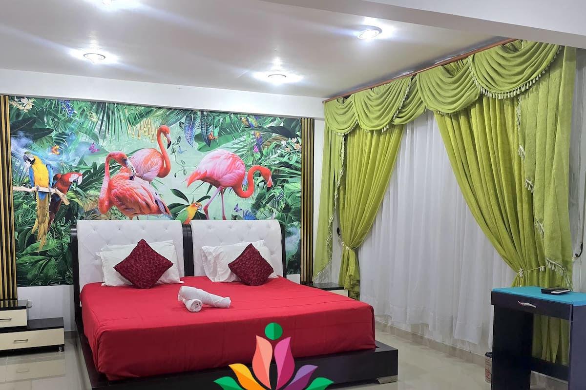 Una suite de hotel con una cama grande, una mesita de noche, un escritorio y un mural de aves y flores tropicales.