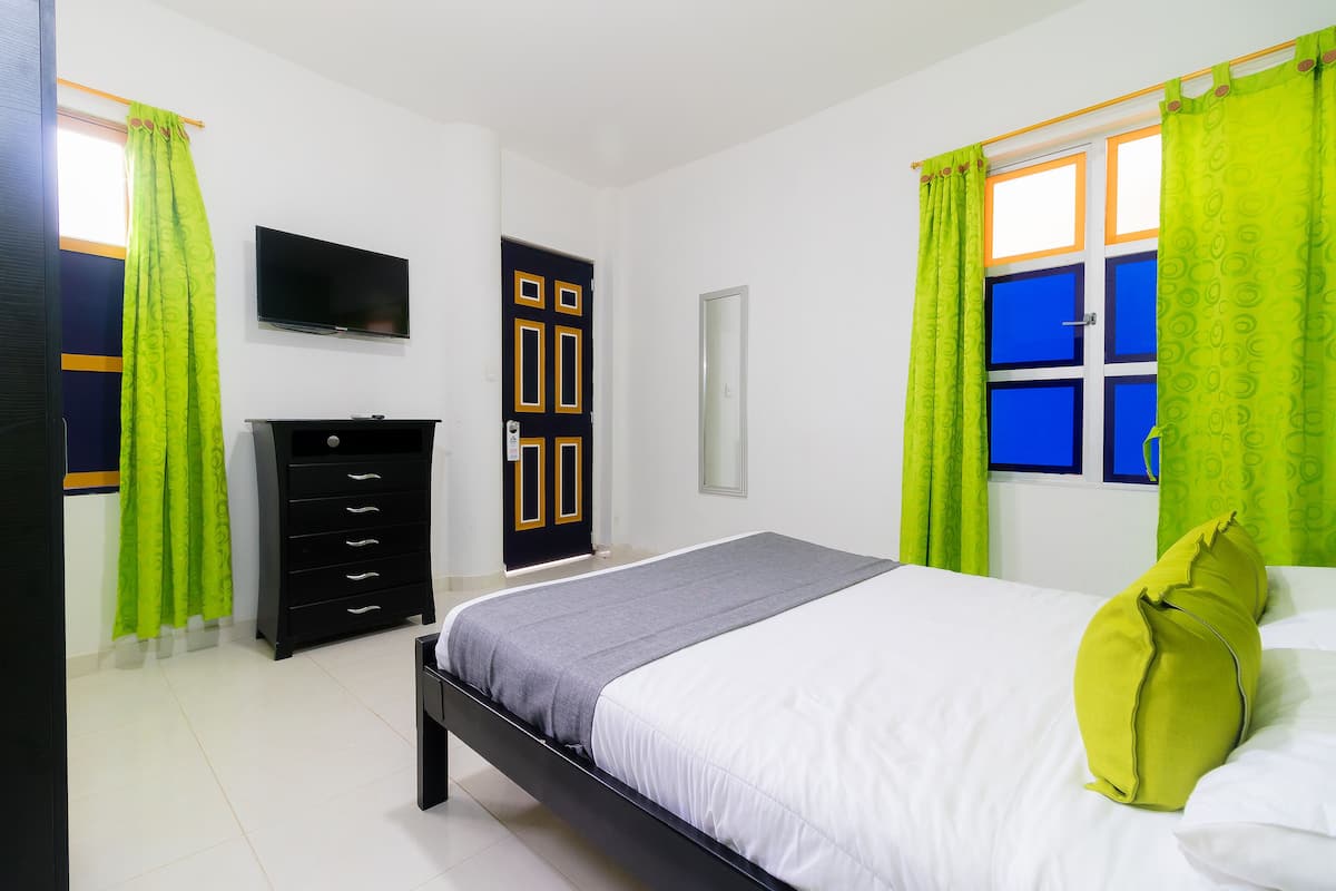 Un dormitorio con cama, televisión, armario y ventana con cortinas.