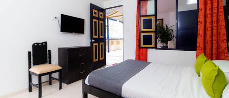 A bedroom with a bed, a desk, a chair, a television, and a window with curtains.