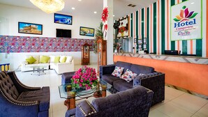 Un hall d’hôtel comprenant un comptoir d’accueil, des canapés, un lustre et des œuvres d’art décoratives murales.