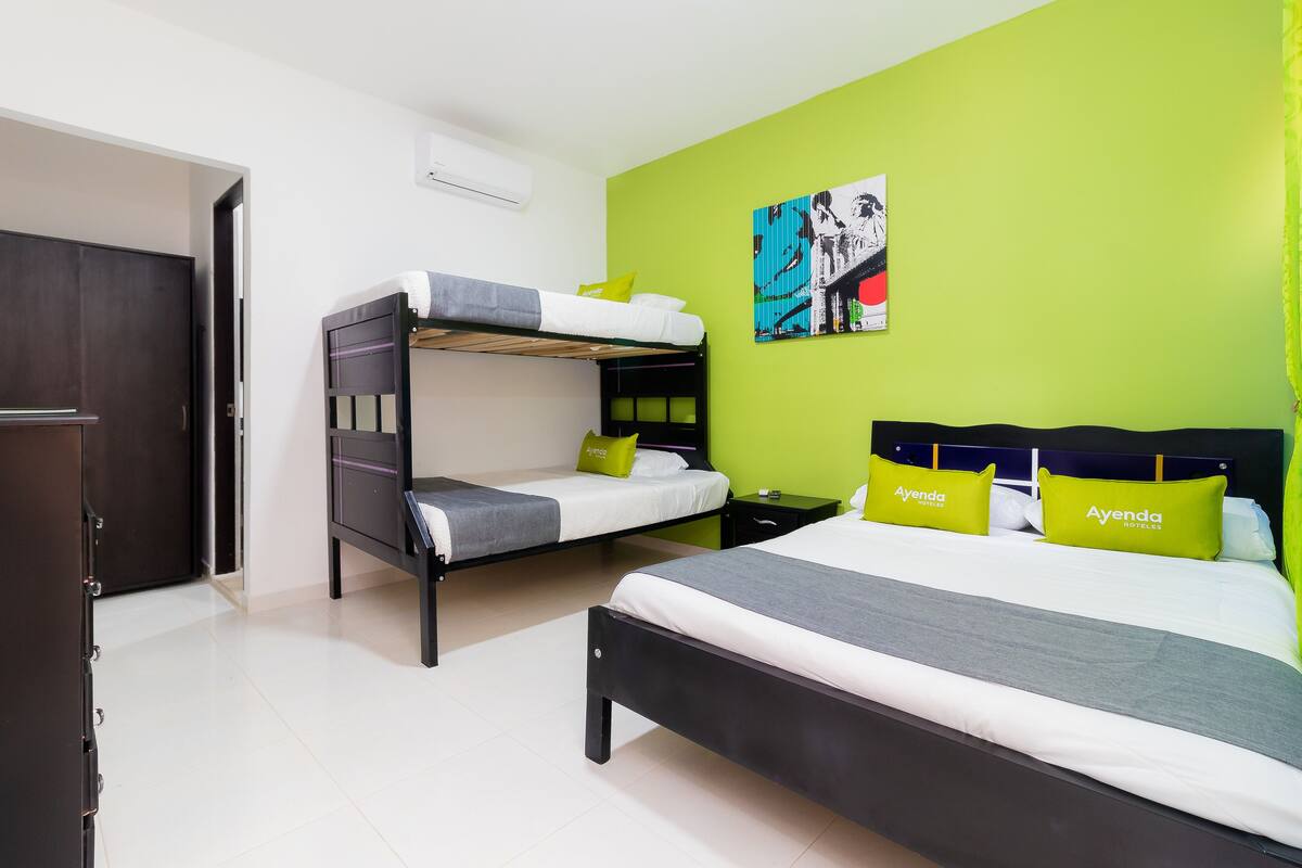 Una habitación de hotel con una cama litera, una cama individual y una pared de acento verde.