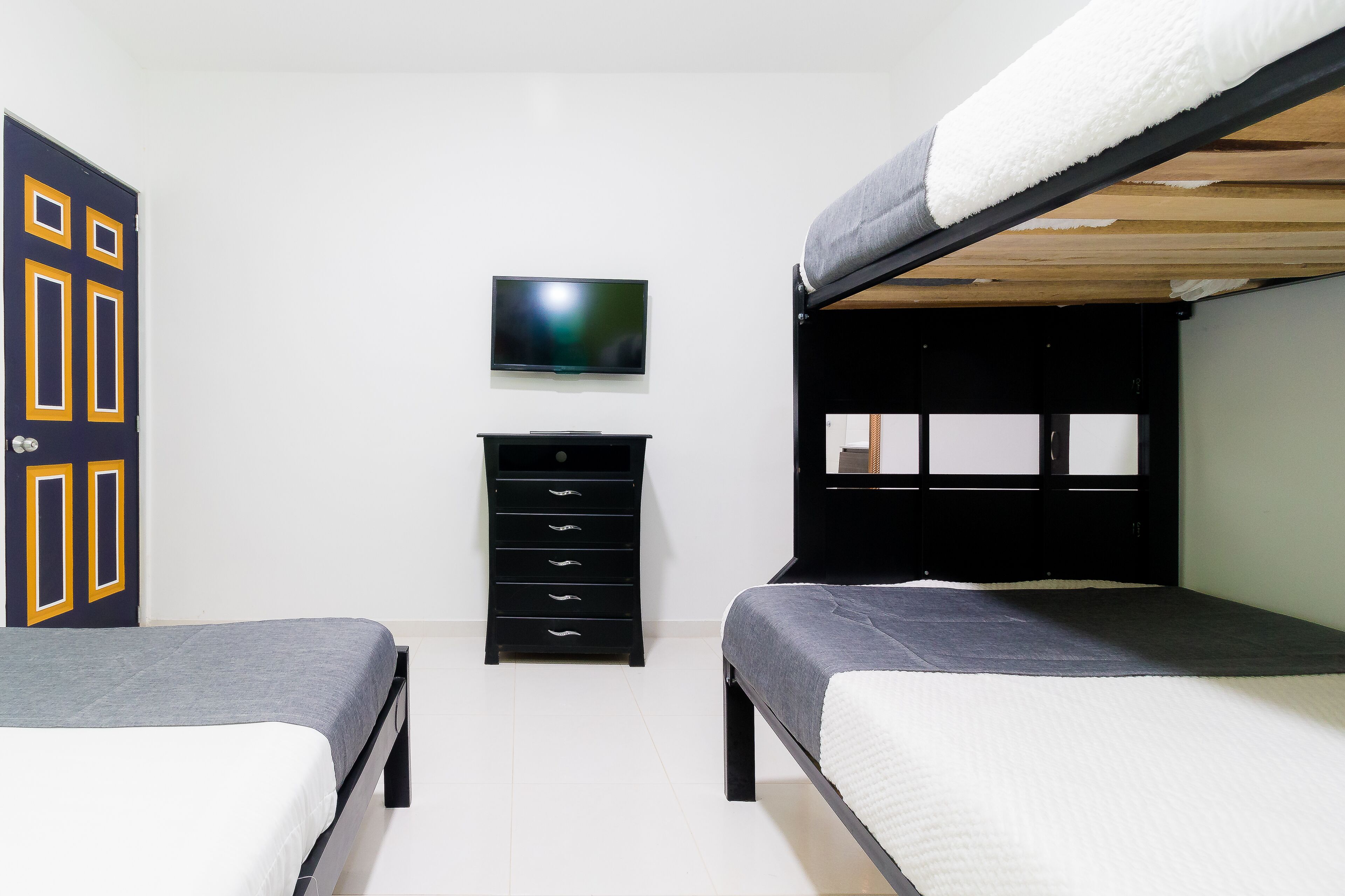 A room with two bunk beds, a flat-screen TV, a black dresser with drawers, and a door with geometric patterns.