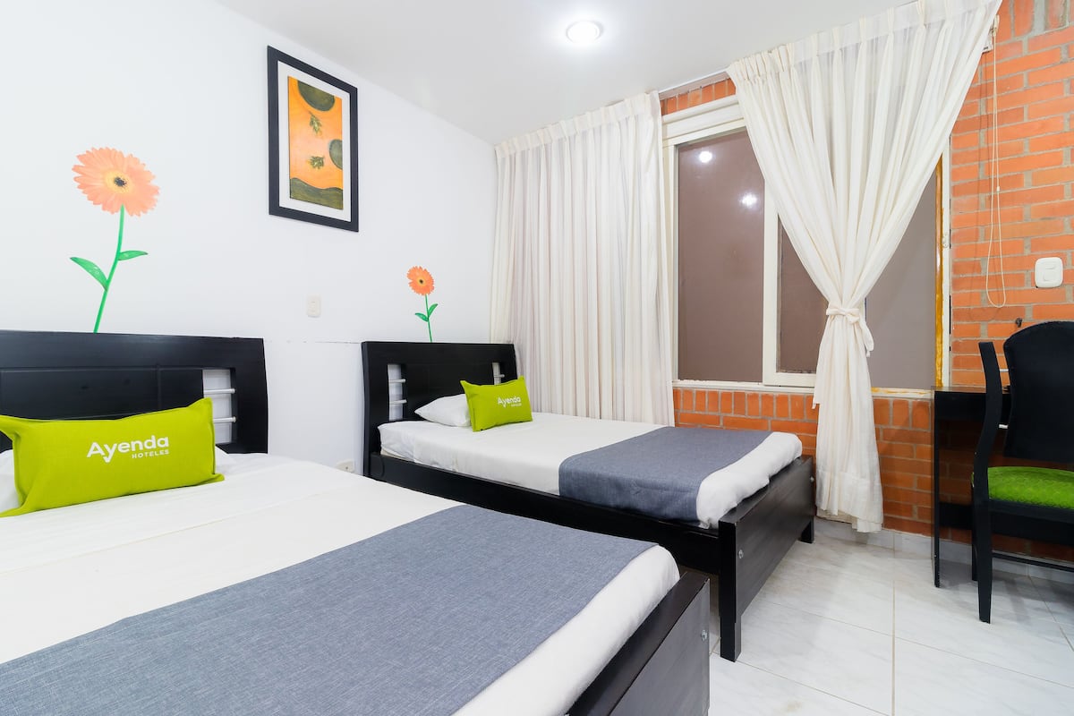 Una habitación de hotel con dos camas, un escritorio, una silla y un ventanal con cortinas.