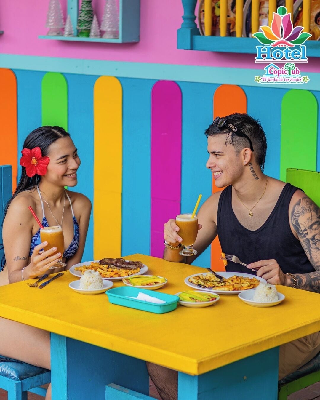 Uma área de refeições vibrante, com uma mesa amarela, diversos pratos e bebidas.