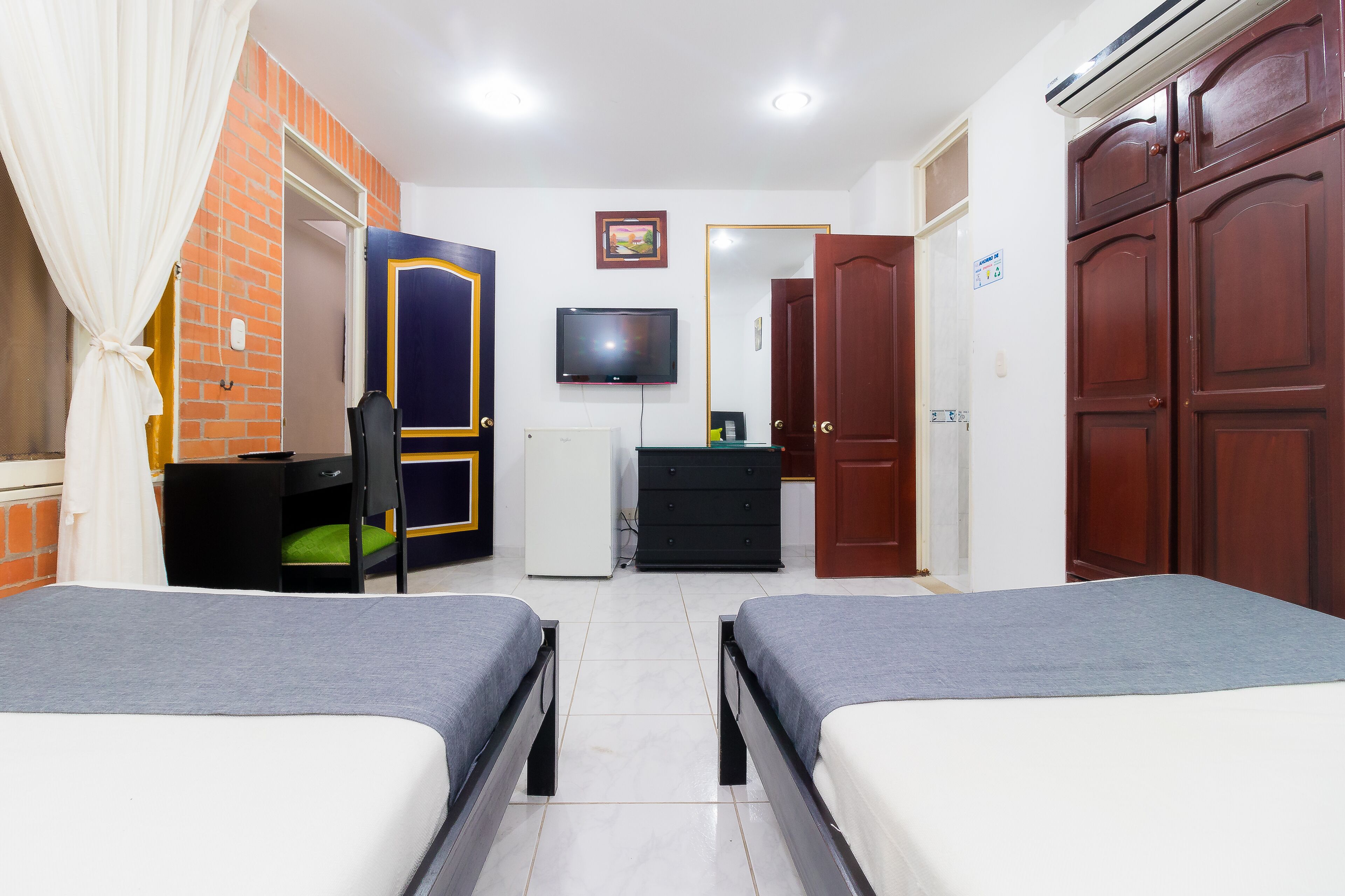 A hotel room with two beds, a TV, a wardrobe, and a desk.
