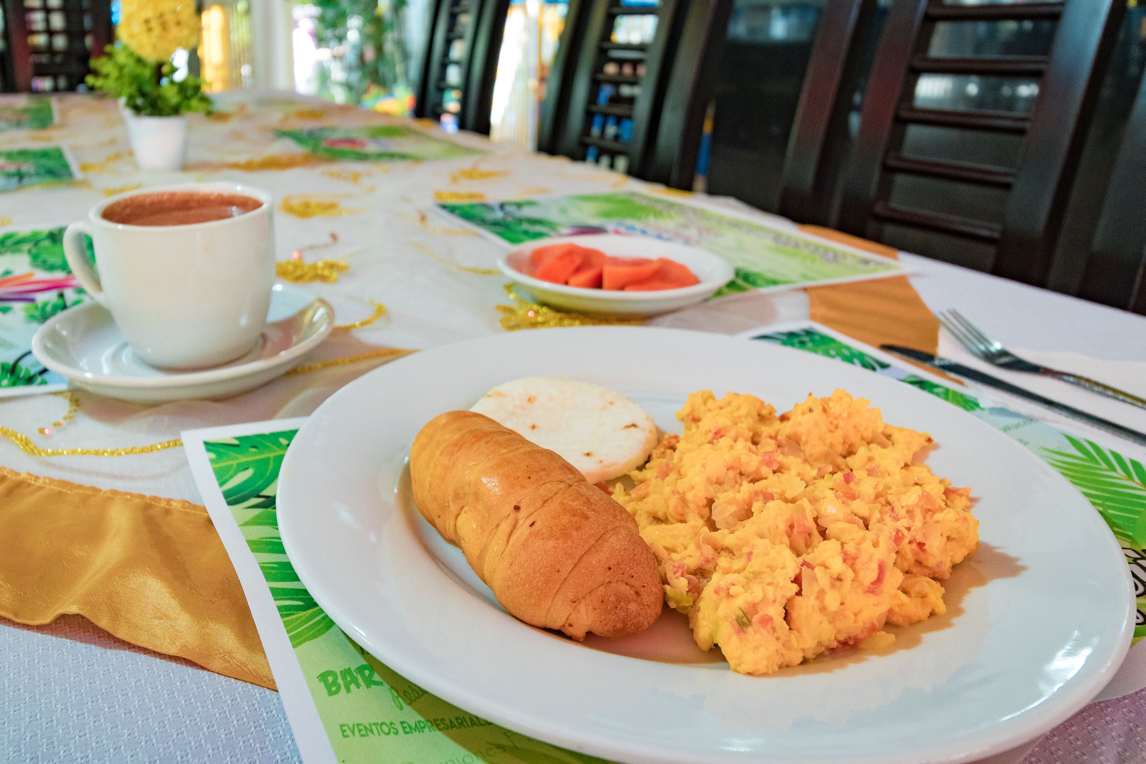 Une table à manger avec une assiette d’œufs brouillés, un croissant et une tasse de café.