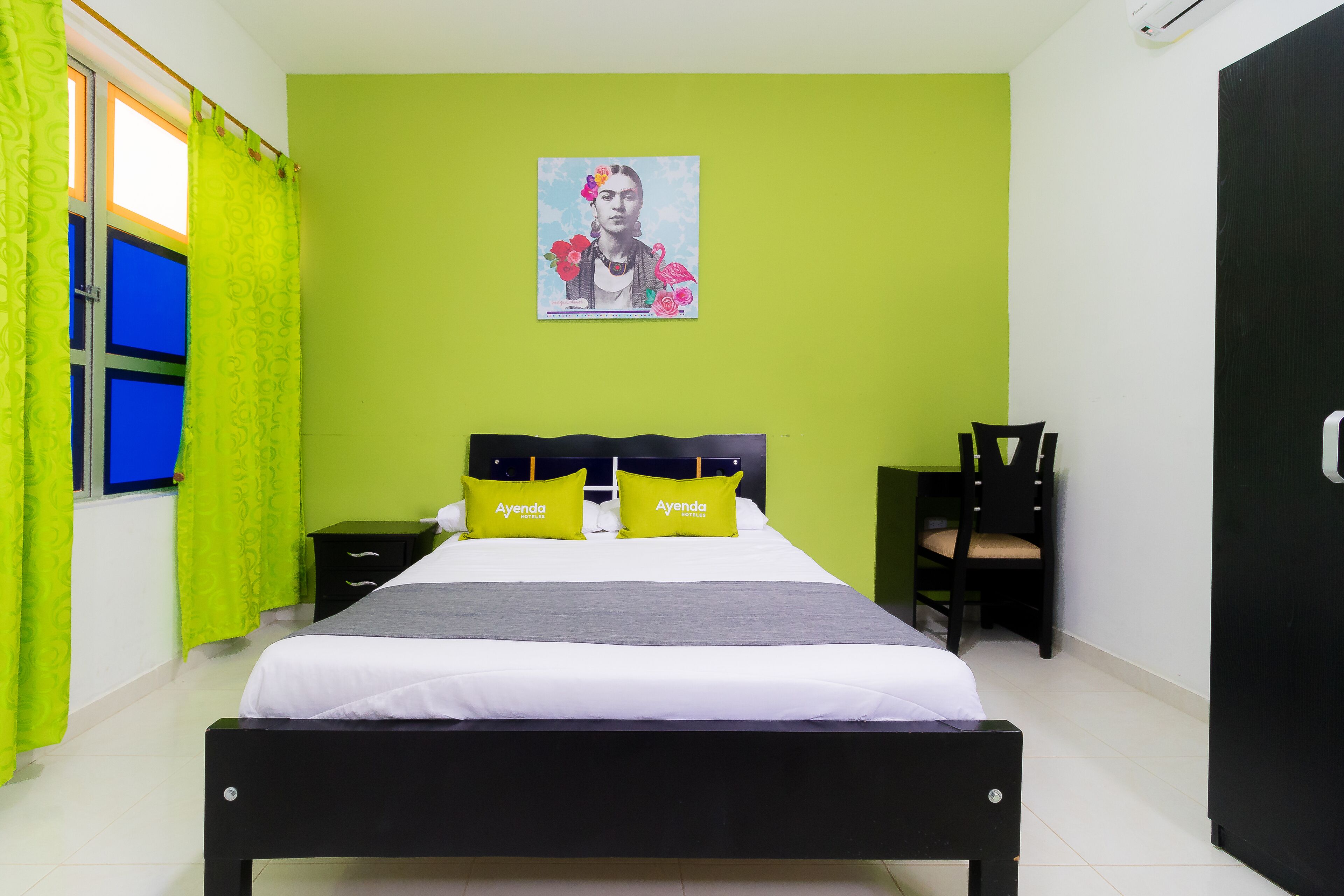 A hotel room with a bed, two nightstands, a chair, a green wall, and a poster.