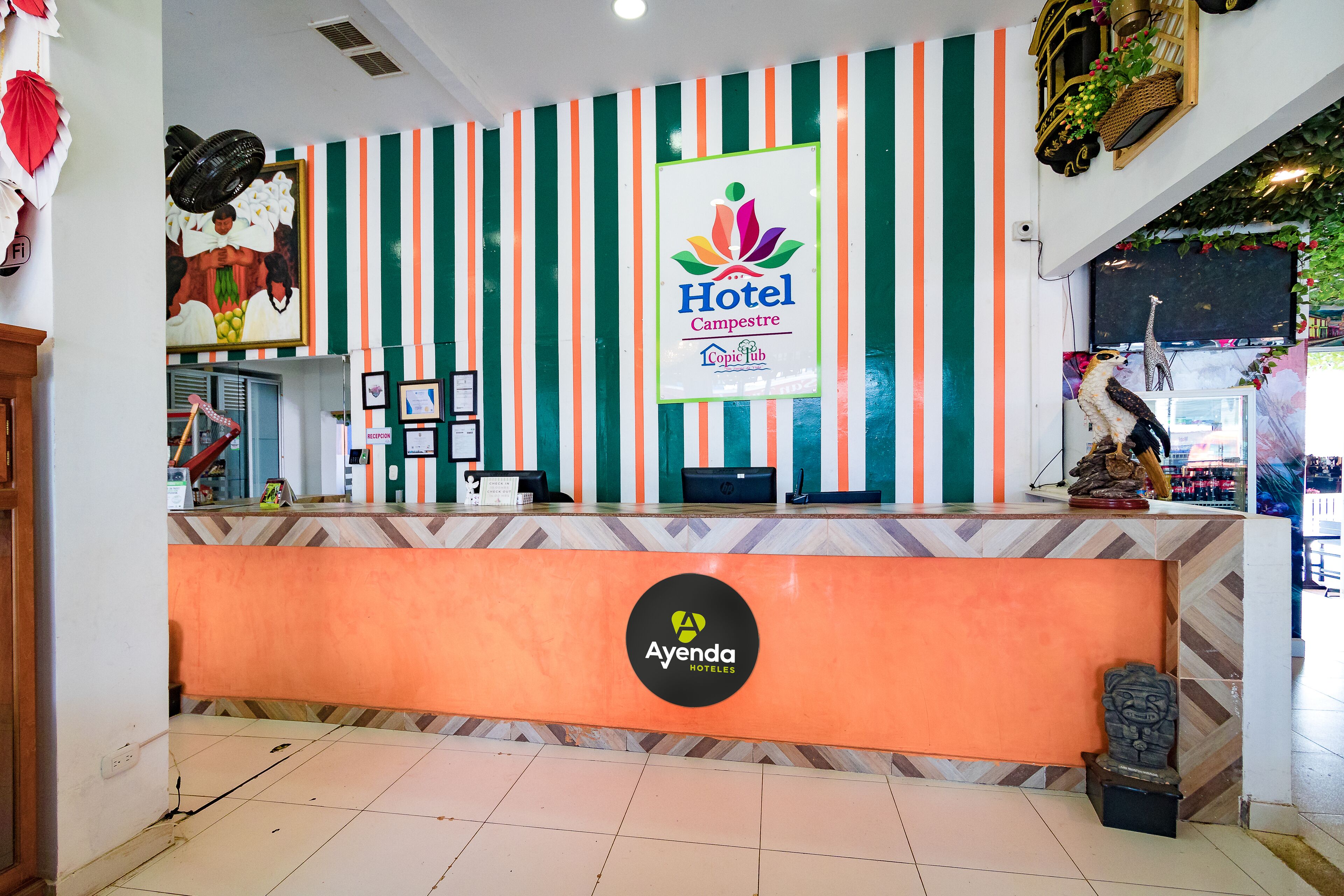 A hotel reception area with a striped wall, a reception desk, and a logo for 'Ayenda Hotels'.