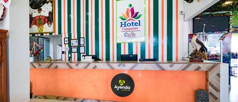 A hotel reception area with a striped wall, a reception desk, and a logo for 'Ayenda Hotels'.