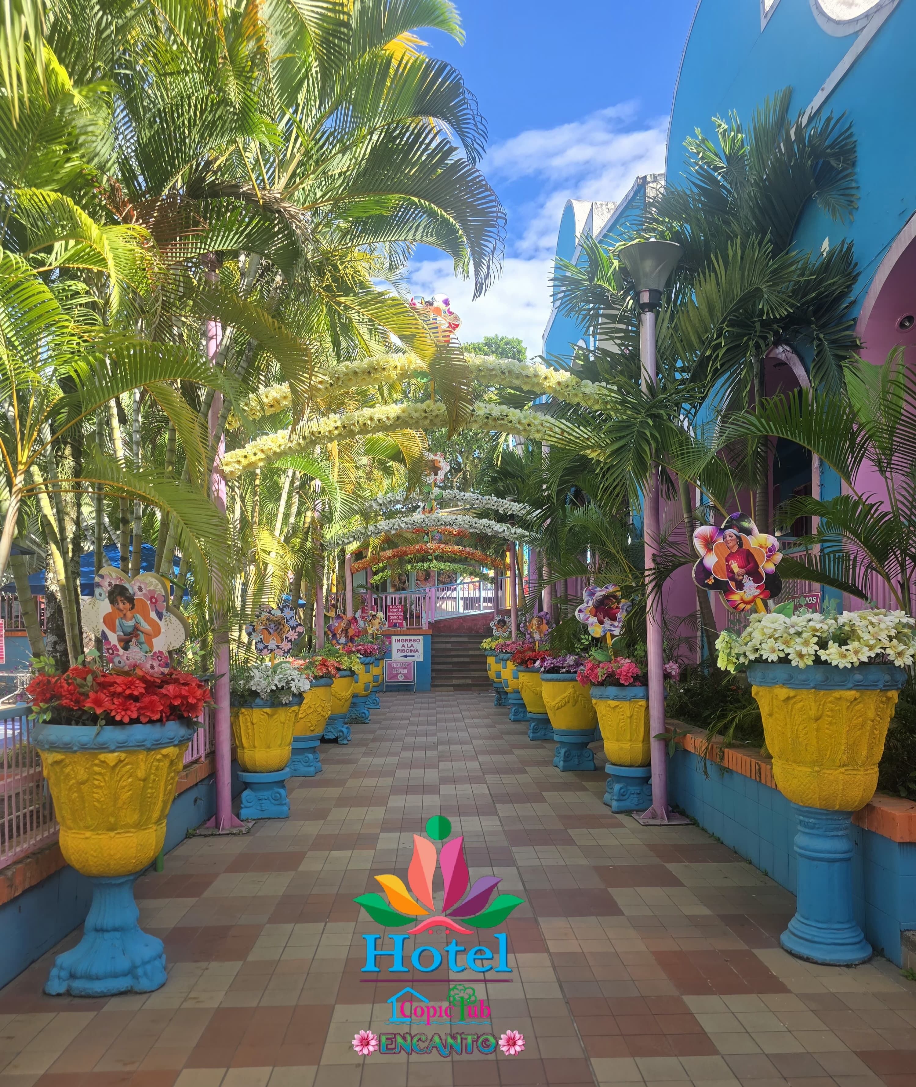 A hotel corridor with a tiled floor, potted plants, and a sign indicating an entrance to a pool area.