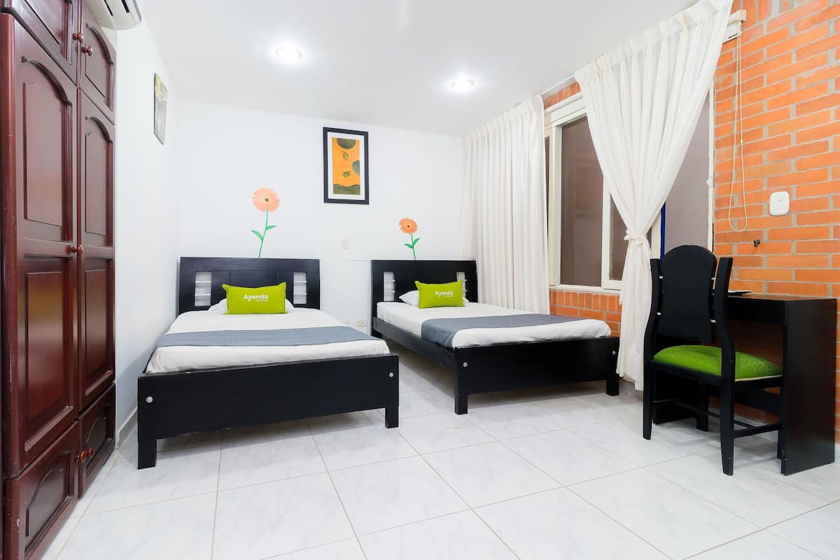 Una habitación con dos camas, un escritorio, una silla, un armario y una ventana con cortinas.